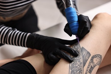 Professional artist tattooing woman's leg with machine in salon, closeup