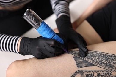 Photo of Professional artist tattooing woman's leg with machine in salon, closeup