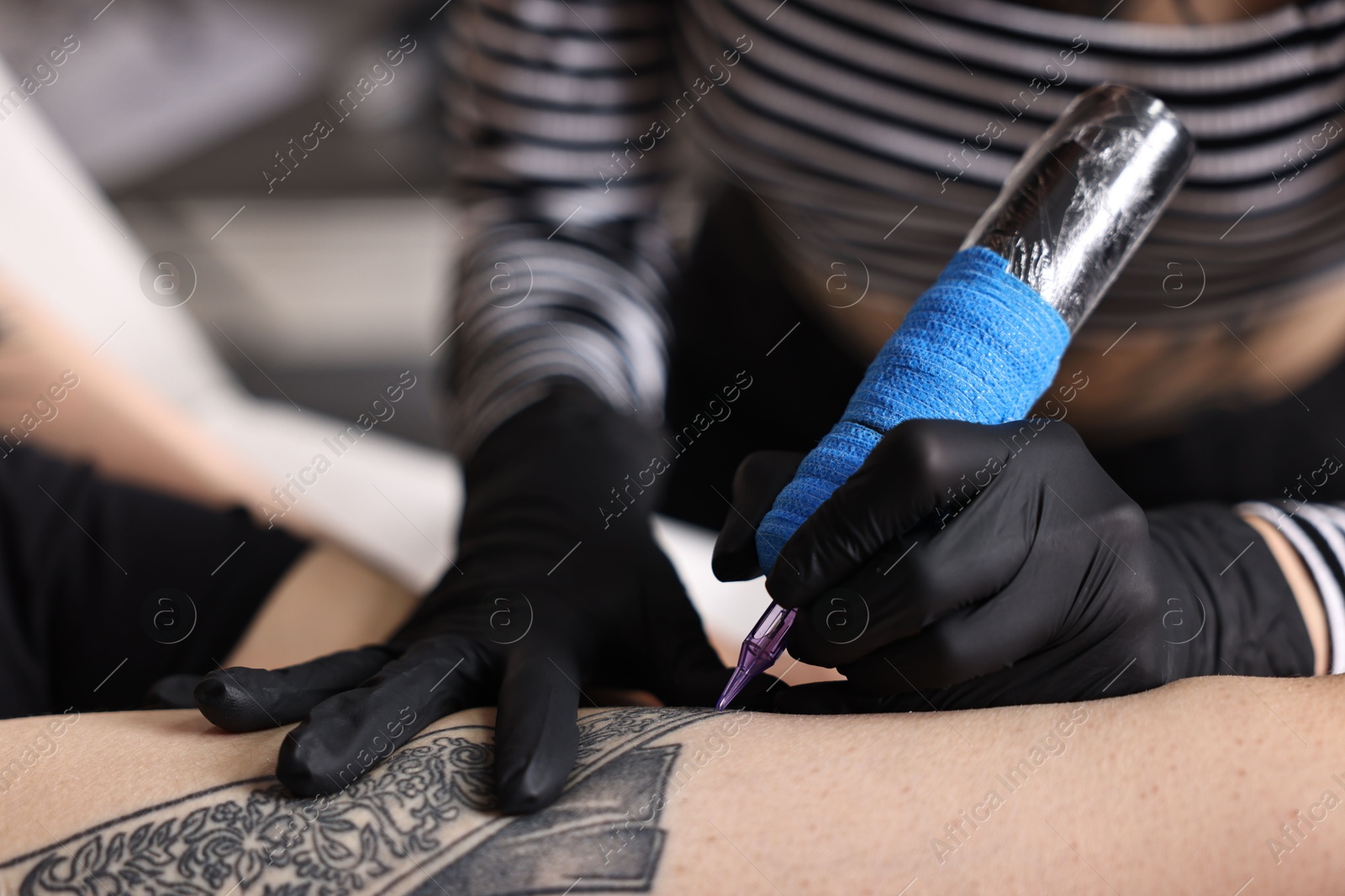 Photo of Professional artist tattooing woman's leg with machine in salon, closeup