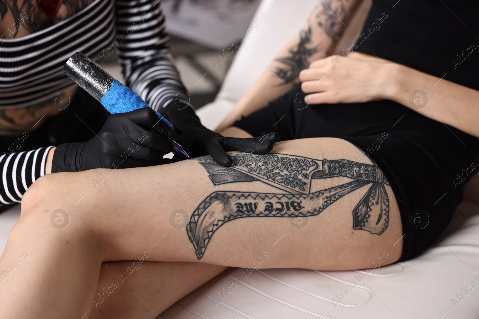 Photo of Professional artist tattooing woman's leg with machine in salon, closeup