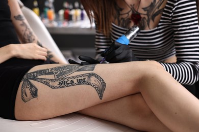 Photo of Professional artist tattooing woman's leg with machine in salon, closeup