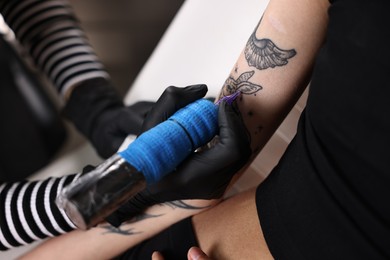 Photo of Professional artist tattooing woman's arm with machine in salon, closeup