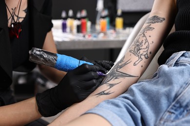 Photo of Professional artist tattooing woman's arm with machine in salon, closeup