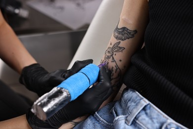 Photo of Professional artist tattooing woman's arm with machine in salon, closeup