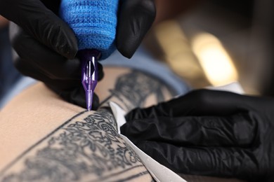 Professional artist tattooing woman with machine in salon, closeup