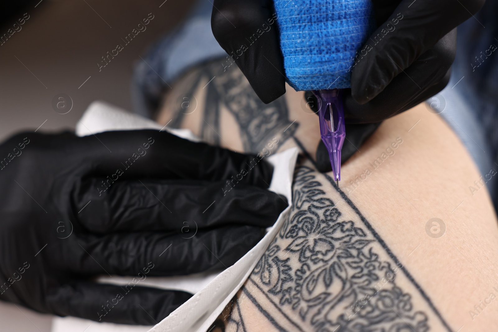 Photo of Professional artist tattooing woman with machine in salon, closeup