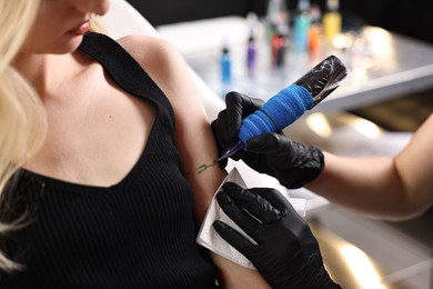 Professional artist tattooing woman's arm with machine in salon, closeup