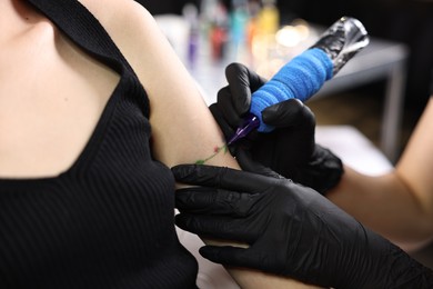 Photo of Professional artist tattooing woman's arm with machine in salon, closeup