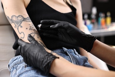 Professional artist in gloves applying cream onto woman's arm with fresh tattoo in salon, closeup