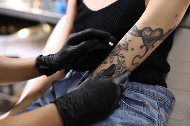 Photo of Professional artist in gloves applying cream onto woman's arm with fresh tattoo in salon, closeup