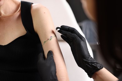 Photo of Professional artist in gloves applying cream onto woman's arm with fresh tattoo in salon, closeup