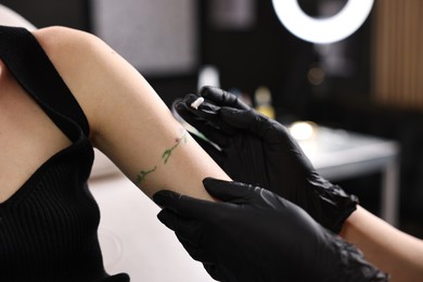 Photo of Professional artist in gloves applying cream onto woman's arm with fresh tattoo in salon, closeup