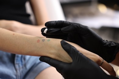 Professional artist in gloves applying cream onto woman's hand with fresh tattoo in salon, closeup