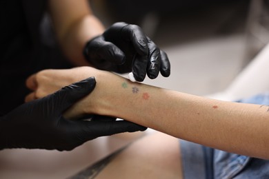 Photo of Professional artist in gloves applying cream onto woman's hand with fresh tattoo in salon, closeup