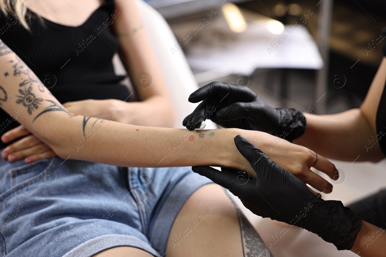 Photo of Professional artist in gloves applying cream onto woman's hand with fresh tattoo in salon, closeup