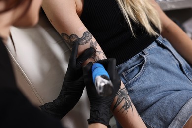 Photo of Professional artist tattooing woman's arm with machine in salon, closeup