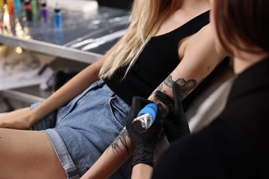 Professional artist tattooing woman's arm with machine in salon, closeup