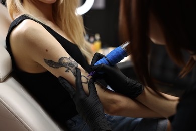 Photo of Professional artist tattooing woman's arm with machine in salon, closeup