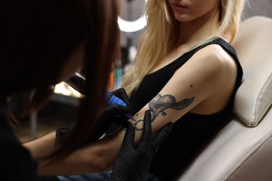 Photo of Professional artist tattooing woman's arm with machine in salon, closeup