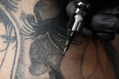 Photo of Artist in glove tattooing woman with machine, macro view