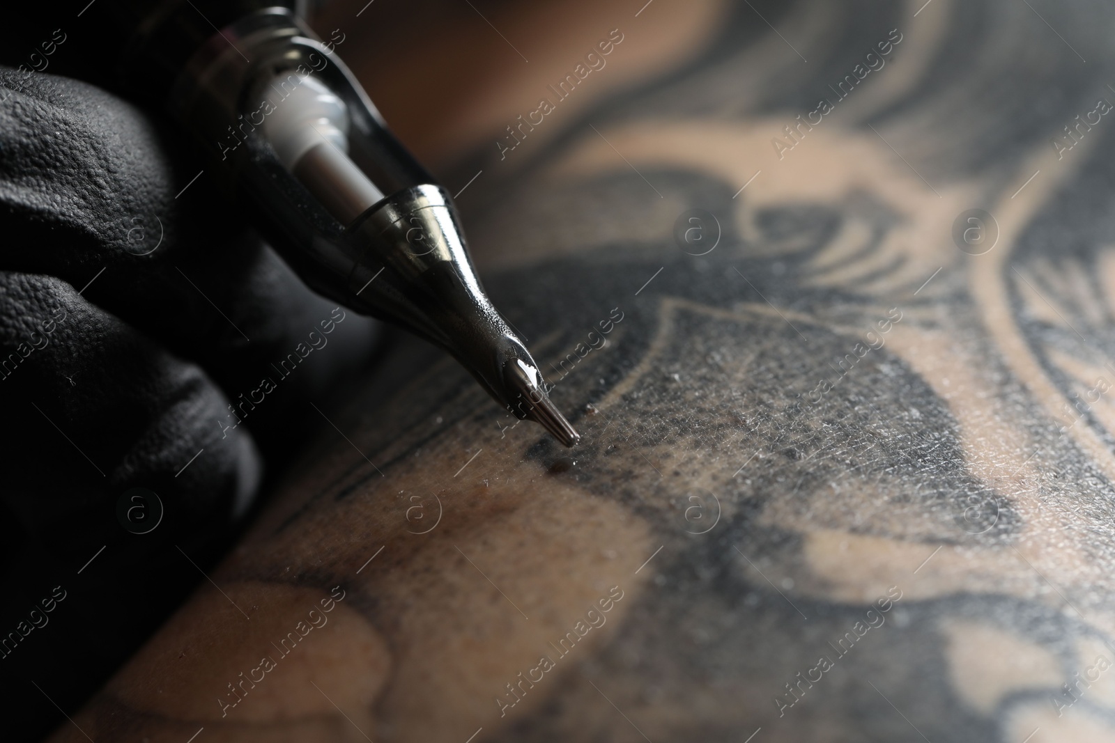 Photo of Artist in glove tattooing woman with machine, macro view