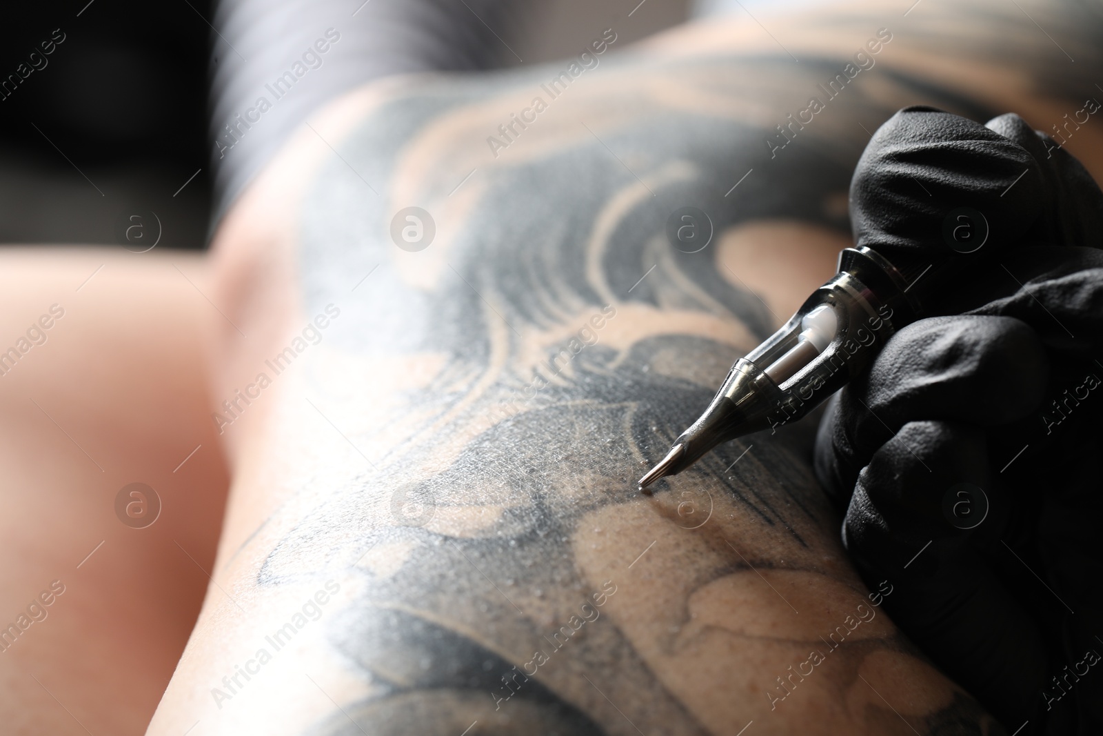 Photo of Artist in glove tattooing woman with machine, macro view