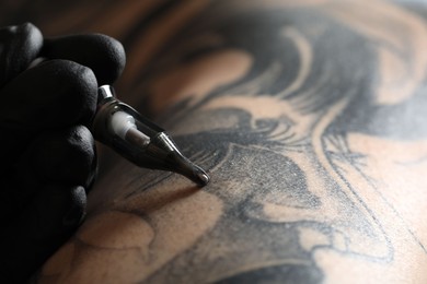 Artist in glove tattooing woman with machine, macro view