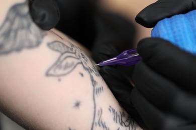 Photo of Artist in glove tattooing woman with machine, macro view