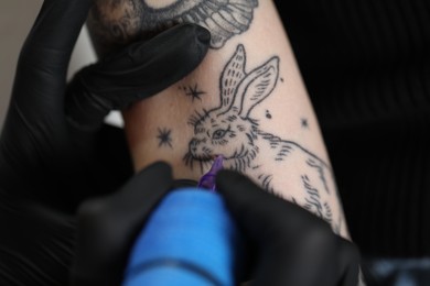 Photo of Artist in glove tattooing woman with machine, closeup