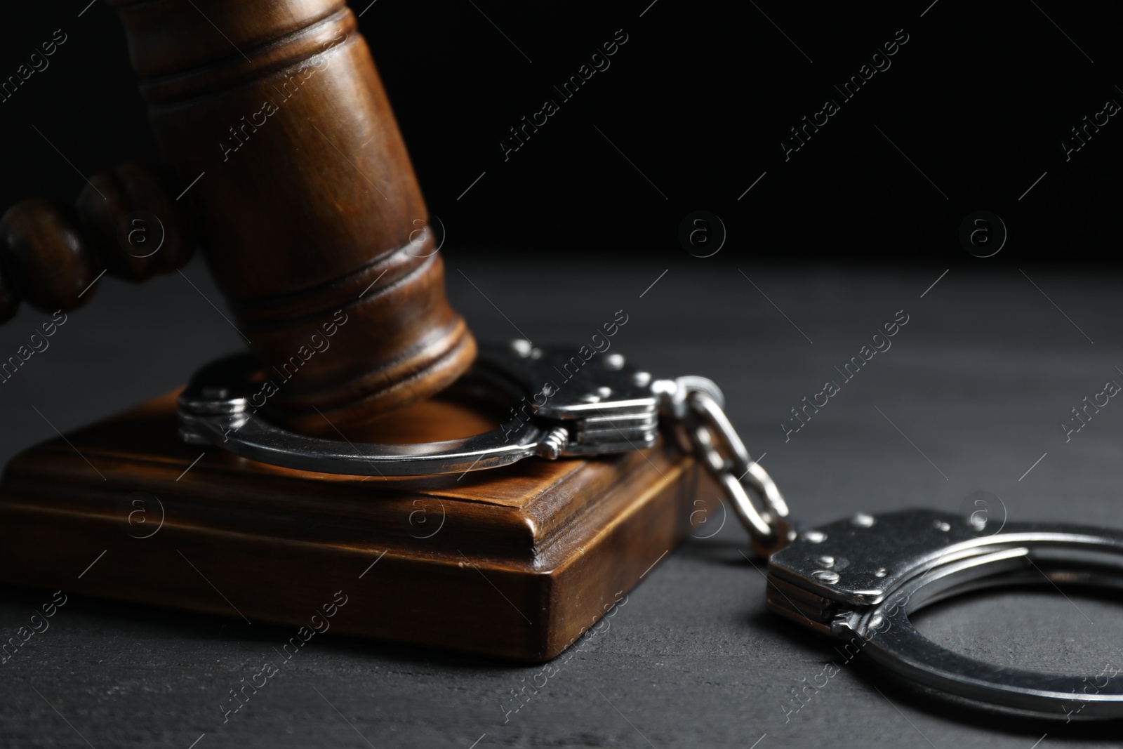 Photo of Handcuffs and judge's gavel on black wooden table, closeup