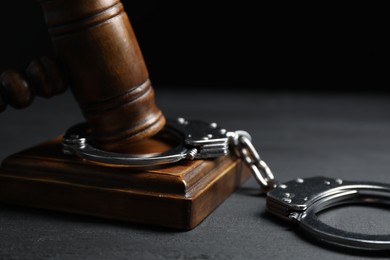 Photo of Handcuffs and judge's gavel on black wooden table, closeup