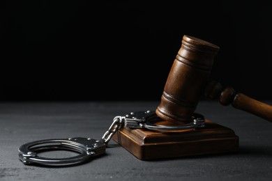 Photo of Handcuffs and judge's gavel on black wooden table, closeup