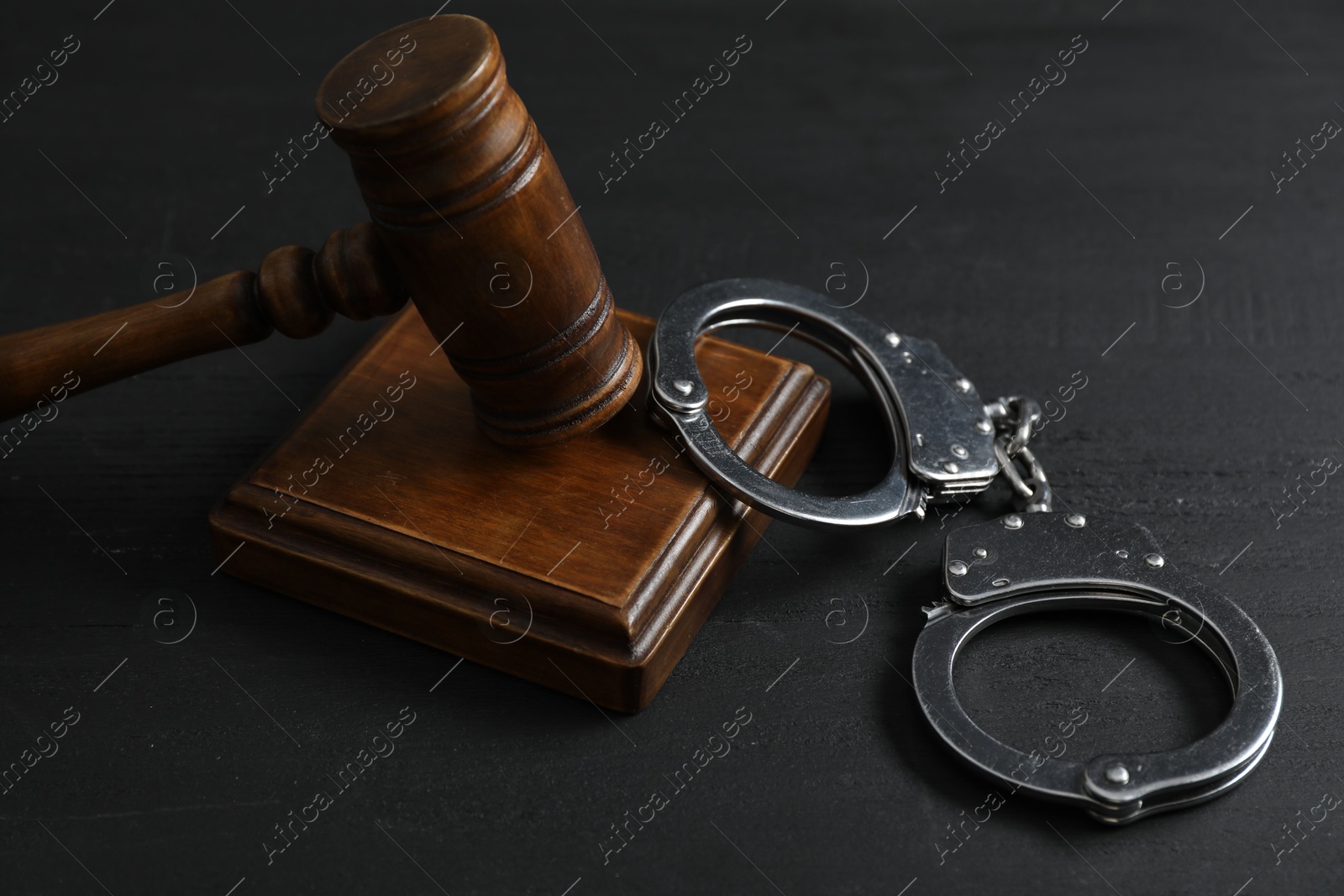 Photo of Handcuffs and judge's gavel on black wooden table, closeup