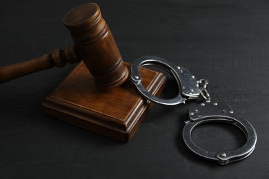 Handcuffs and judge's gavel on black wooden table, closeup