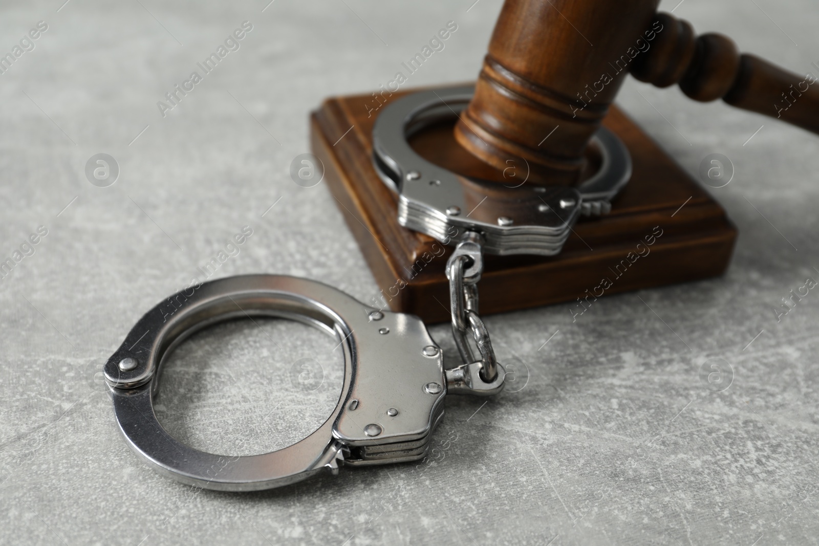 Photo of Handcuffs and judge's gavel on grey textured table, closeup