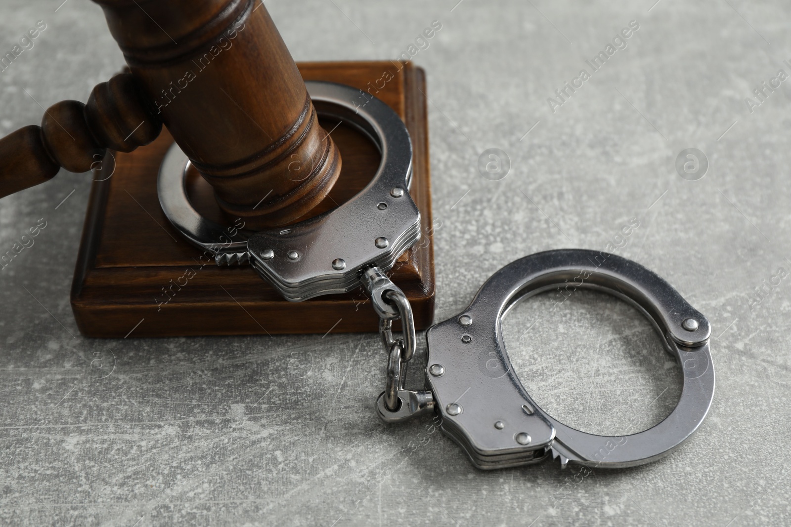 Photo of Handcuffs and judge's gavel on grey textured table, closeup