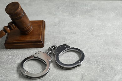 Handcuffs and judge's gavel on grey textured table, space for text