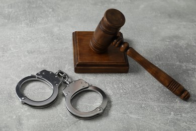 Handcuffs and judge's gavel on grey textured table