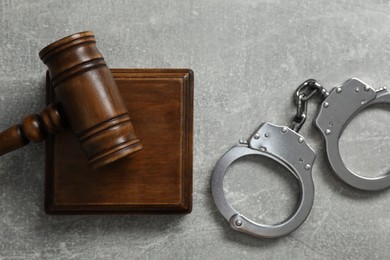 Handcuffs and judge's gavel on grey textured table, flat lay