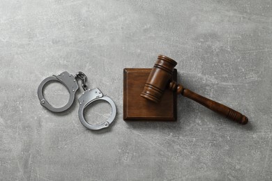 Handcuffs and judge's gavel on grey textured table, flat lay