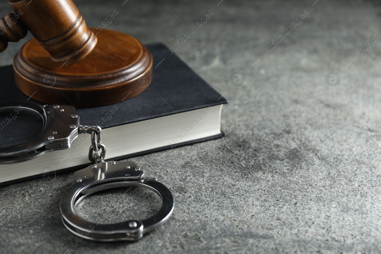 Photo of Handcuffs, book and judge's gavel on grey textured table, closeup. Space for text