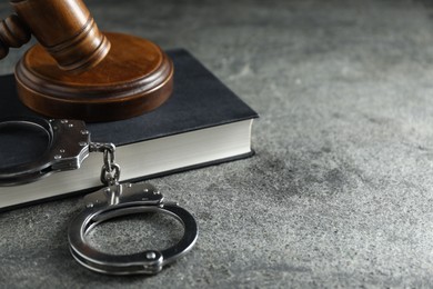 Handcuffs, book and judge's gavel on grey textured table, closeup. Space for text