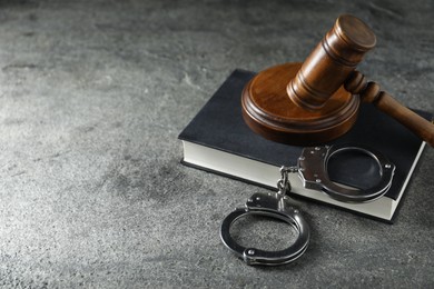 Handcuffs, book and judge's gavel on grey textured table, space for text