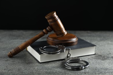 Handcuffs, book and judge's gavel on grey textured table, closeup