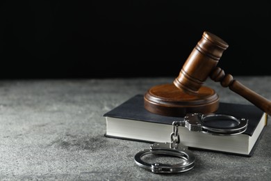 Handcuffs, book and judge's gavel on grey textured table, space for text