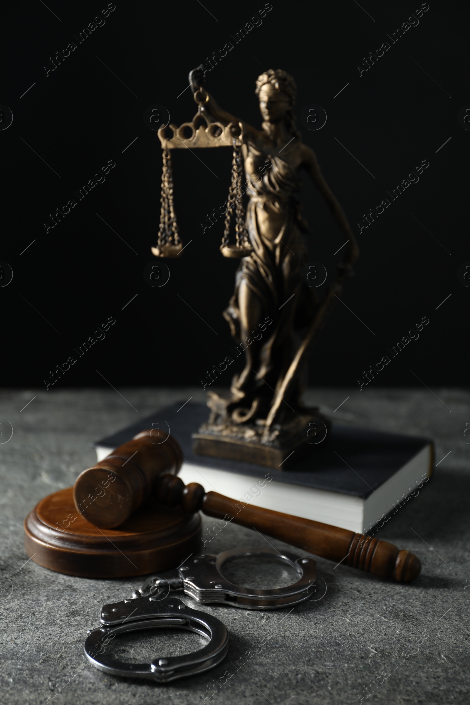 Photo of Handcuffs, judge's gavel, Lady Justice figure and book on grey textured table