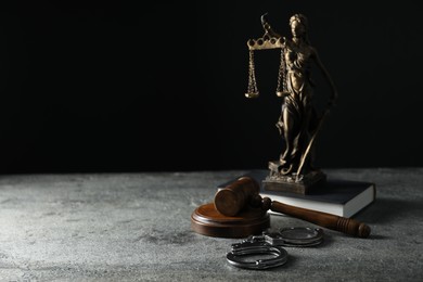 Handcuffs, judge's gavel, Lady Justice figure and book on grey textured table, space for text