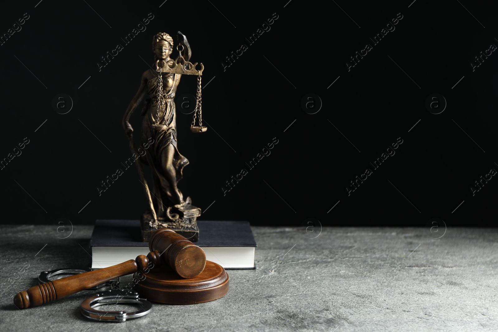 Photo of Handcuffs, judge's gavel, Lady Justice figure and book on grey textured table, space for text