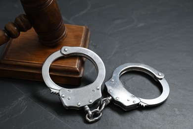 Handcuffs and judge's gavel on grey textured table, closeup