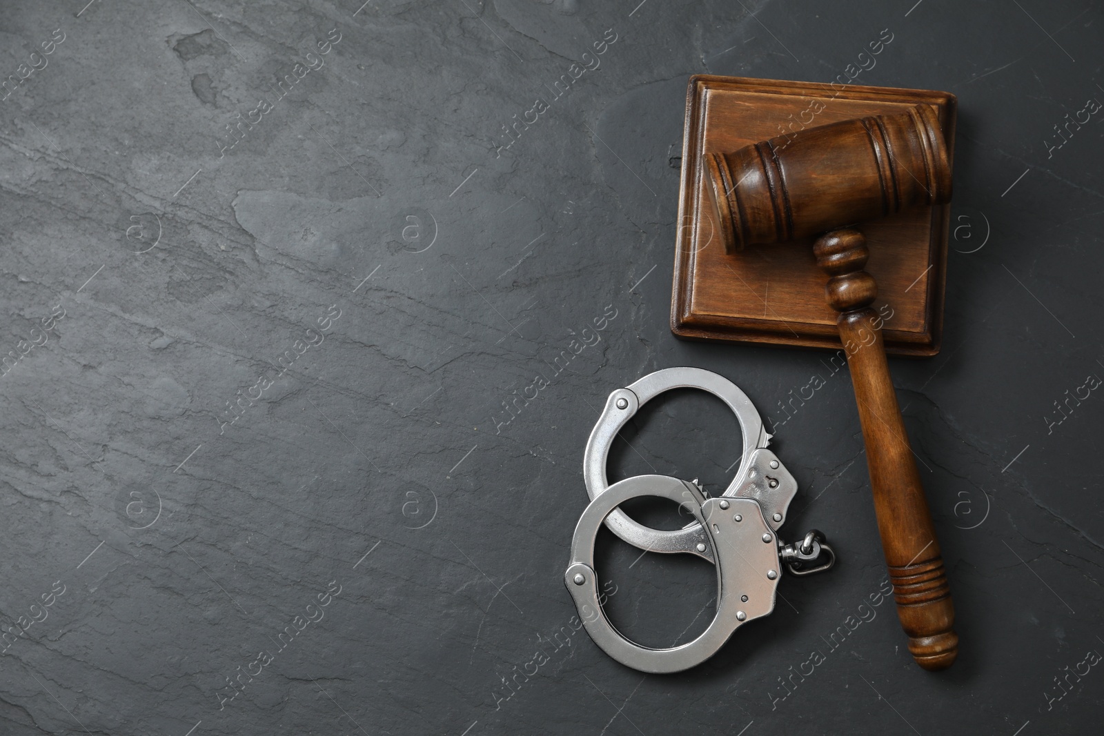 Photo of Handcuffs and judge's gavel on grey textured table, flat lay. Space for text